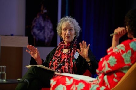 The author Margaret Atwood is seated, raising her hands in animated conversation with Samira Ahmed, seated partly out of frame to the right.