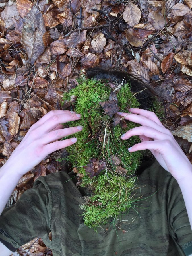 Photo by Louise Ashcroft human body lying on the ground, face covered by moss
