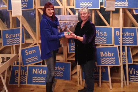 Two women exchanging a seed pouch surrounded by placards with place names on them