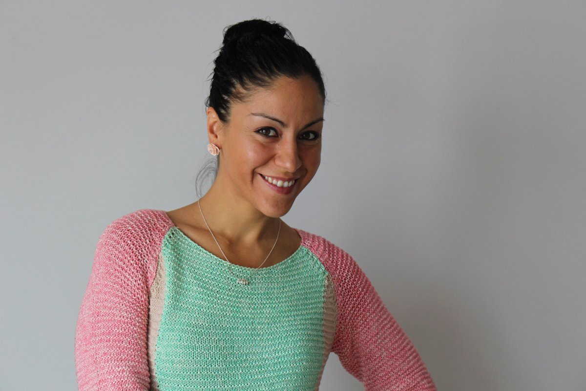 Rose poses in front of a white background, wearing a pale pink and green sweater.