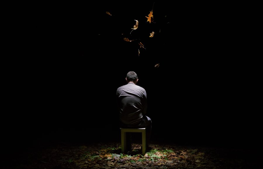 Person sitting in a dark space with a light from above illuminating leaves falling on them