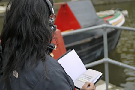 A person with shoulder length hair photographed from behind so face isn't visible is listening to the audio tour while reading a booklet